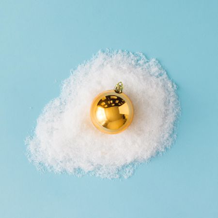 Egg made of golden Christmas bauble decoration and snow on blue background