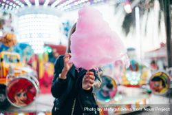 Woman covering face with large cotton candy outside of fairground ride bGm2e5