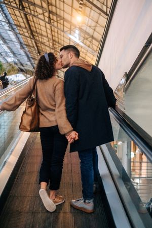 Young couple kissing riding travelator in mall