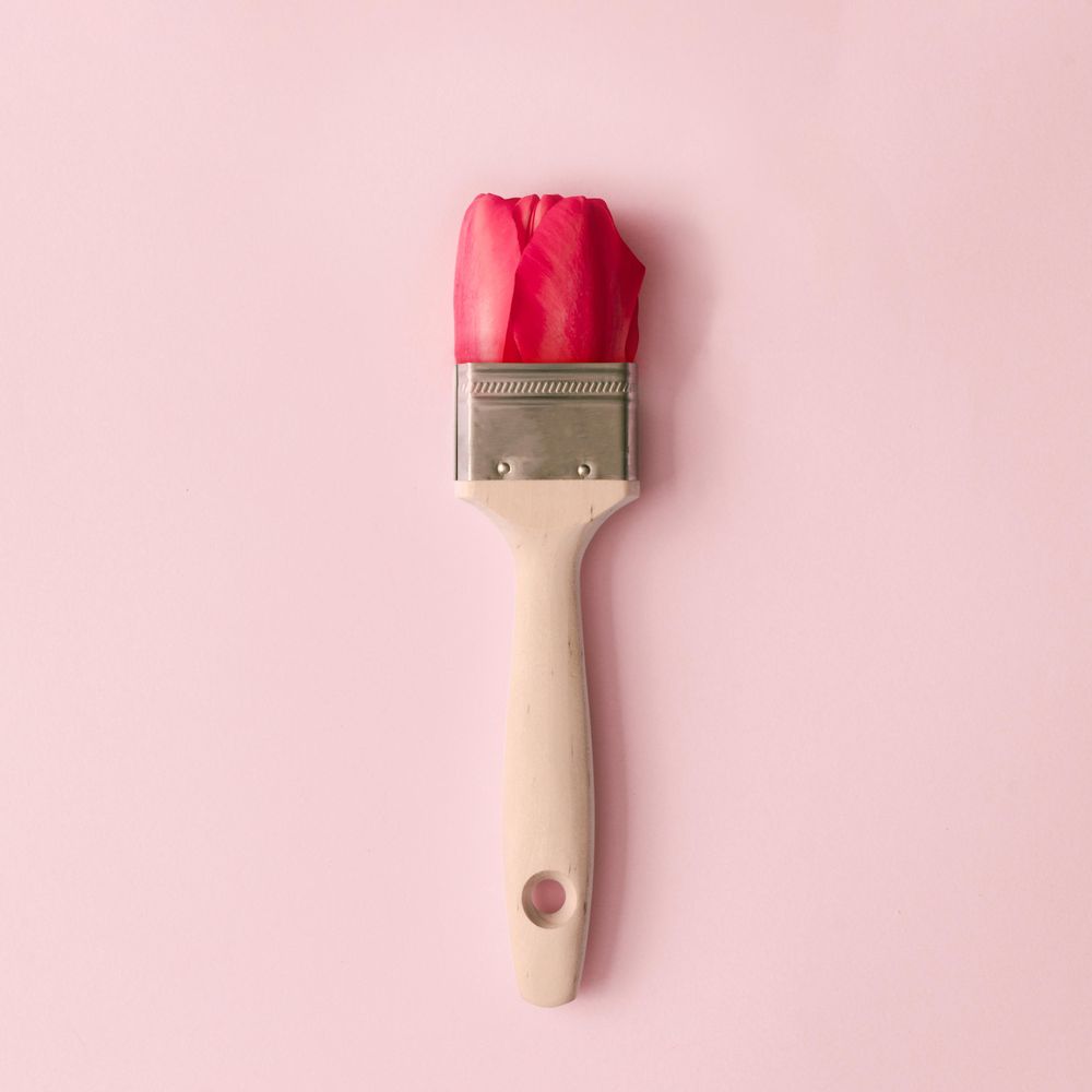 Paint brush and red tulip flower on pastel pink background