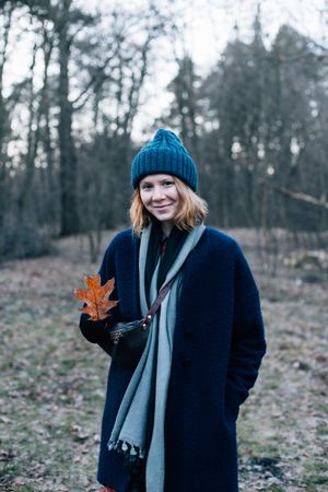 Woman surrounded by trees on cold day with red leaf