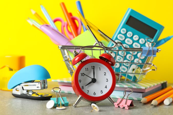 Red alarm clock and back to school supplies in bright yellow background