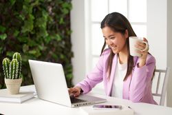 a young asian woman smiling working at the computer in the coworking space having coffee