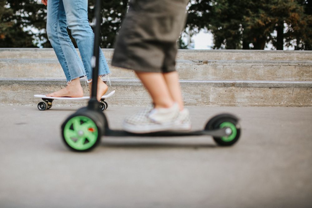 Two children on scooter and skateboard during daytime
