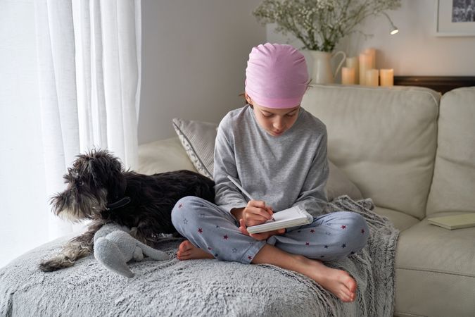 Thoughtful boy in pink scarf writing in notebook near dog