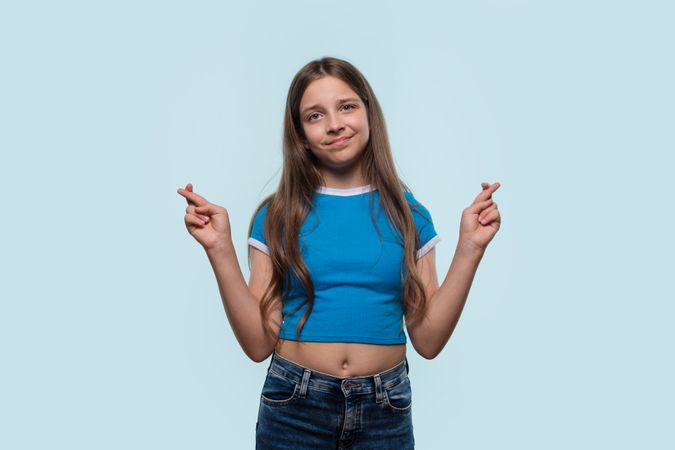 Girl standing with fingers crossed, hoping for good luck.