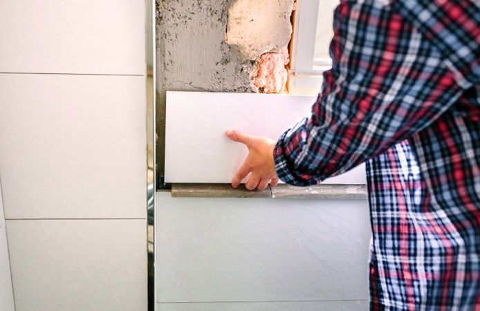 Unrecognizable female bricklayer laying tile on the wall
