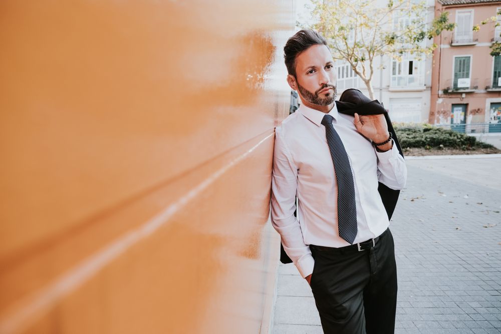Adult smiling stylish man in costume near orange wall on street