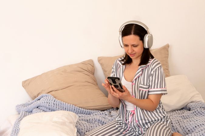 Woman with headphones using smartphone in bed.