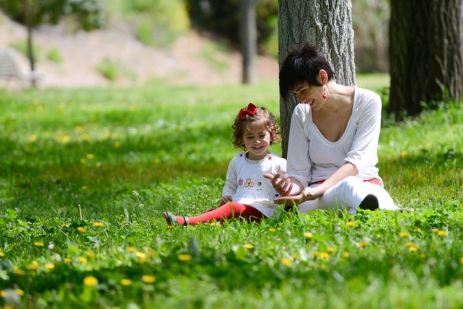 Woman sitting with girl in green sunny park