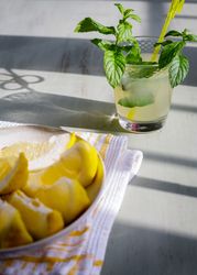 Glass of fresh lemonade next to plate with cut lemons on table