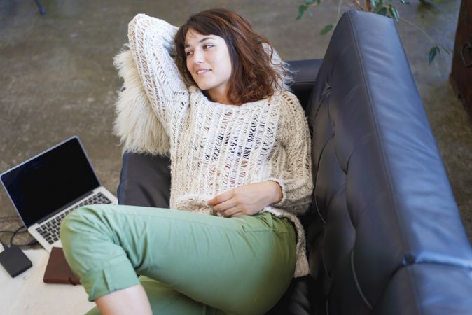 Woman in sweater relaxing on sofa next to laptop
