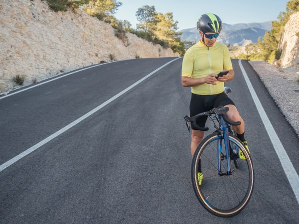 healthy man with smartphone after cycling in a mountain road in a sunny day