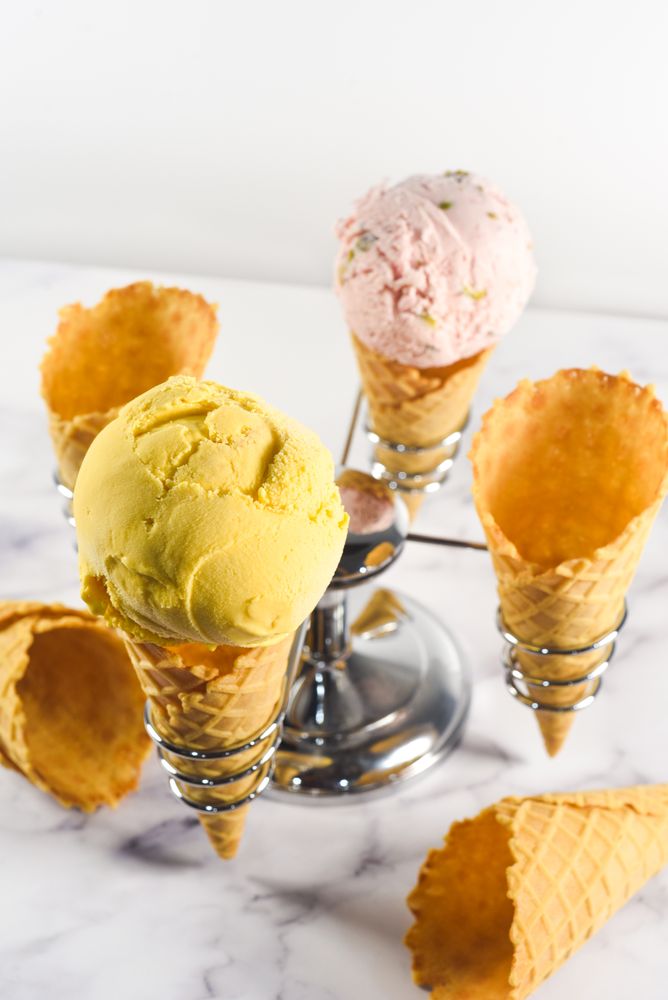Ice cream cone stand with waffle cones and pink and purple scoops, vertical