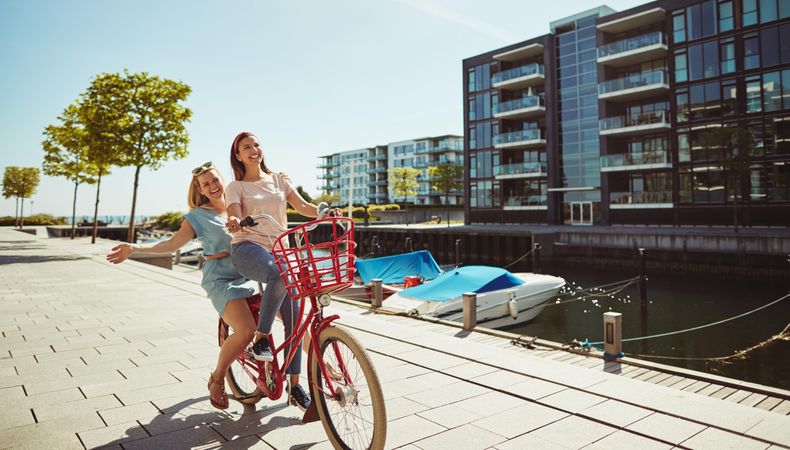 Two close female friends laughing while walking and talking along the waterfront, copy space