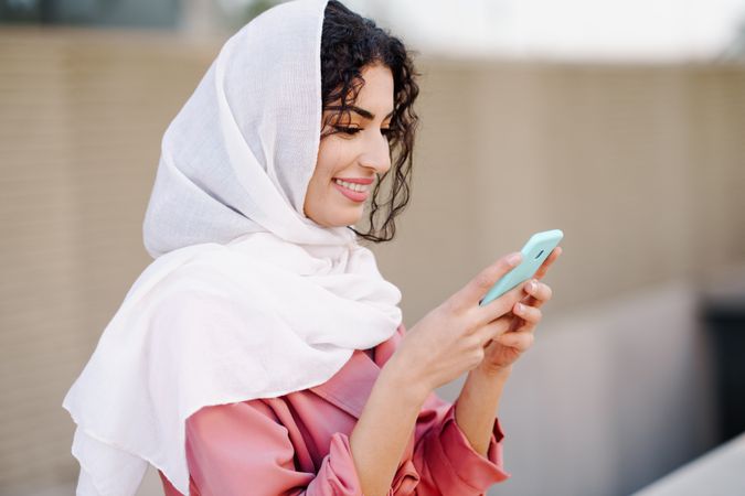 Happy female in headscarf and pink coat with her phone