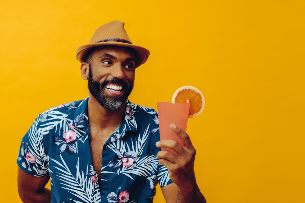 Happy male about to enjoy a cocktail while wearing colorful shirt with yellow background