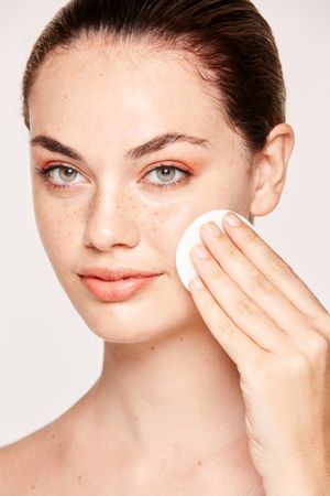 Peaceful female applying toner on radiant face with sponge