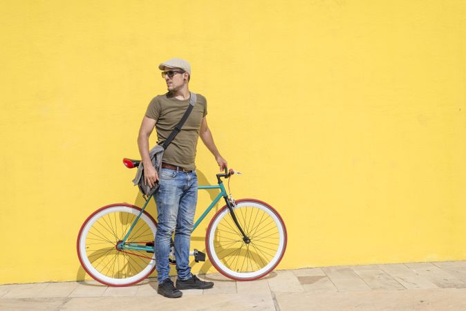 Man in hat standing with bike next to yellow wall