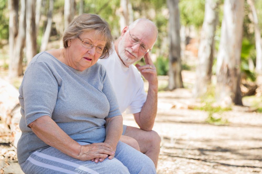 Upset Mature Woman Sits With Concerned Husband Outdoors