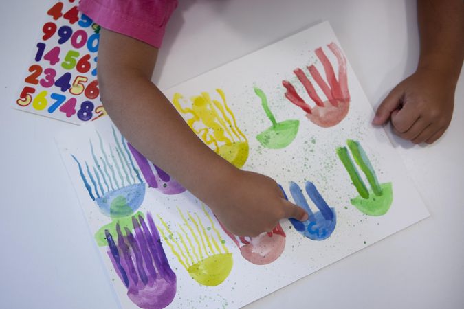 Top view of child's hand painting colorful octopi on paper using water color