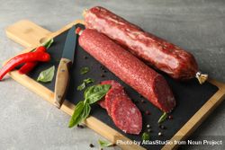 Two sticks of cured meats with slices on wooden board 42ZM14