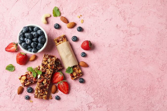 Granola bars and bowl with blueberry on pink background, top view