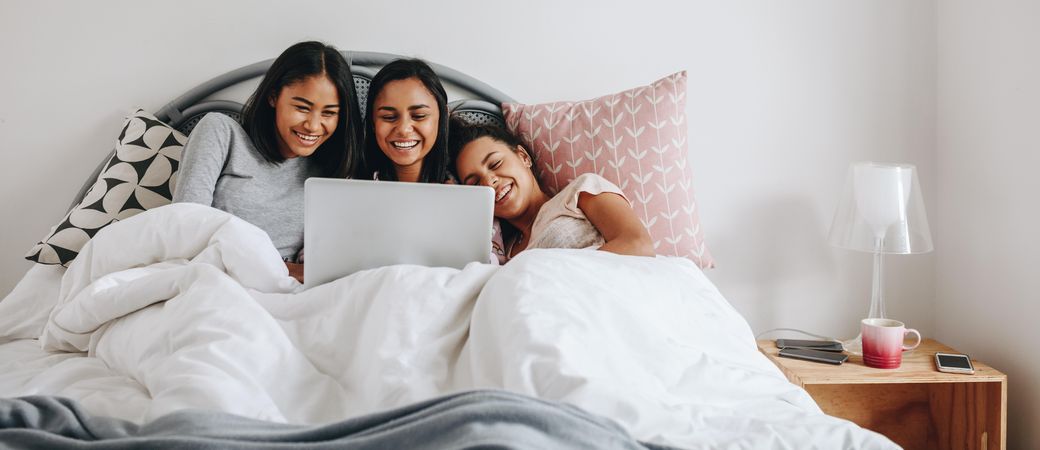Girls having fun using a laptop lying on bed during a sleepover
