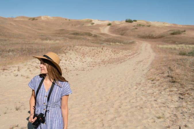 adult woman in straw hat and dress with camera walking on country path