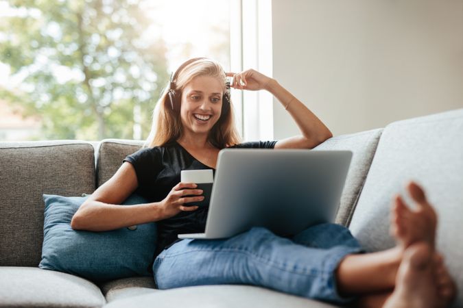 Smiling young woman enjoying a cup of coffee while relaxing with her laptop in living room