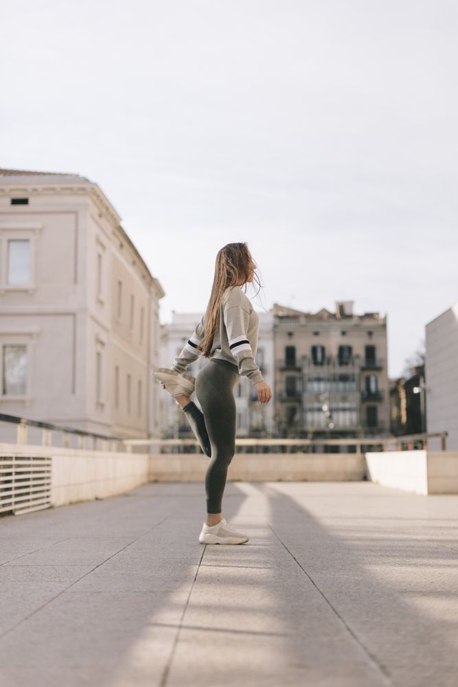 Side view of woman standing and stretching her leg on a city roof top