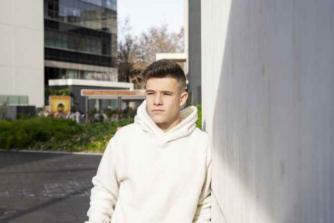 Portrait of young man in bright hoodie leaning on wall outside