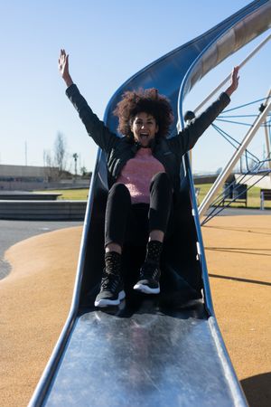 Woman with afro hair jumping down a slide.