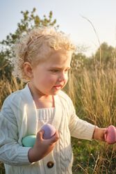 Cute little girl collecting Easter eggs in sunny countryside