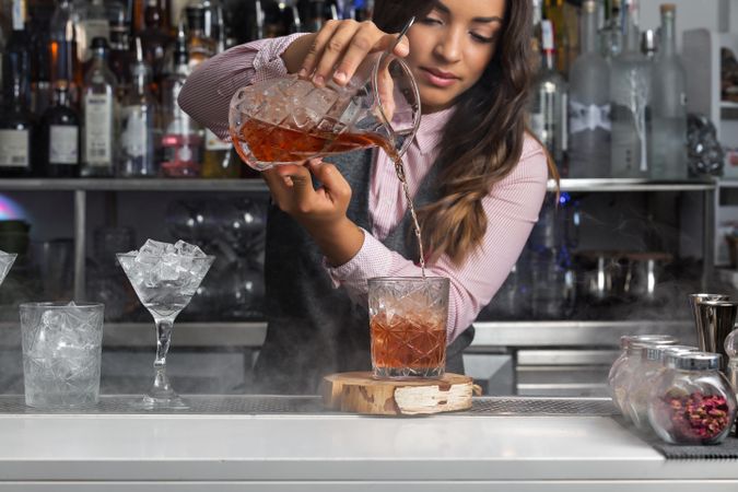 Bartender pouring stirred Negroni cocktail into an old-fashion glass with ice cubes