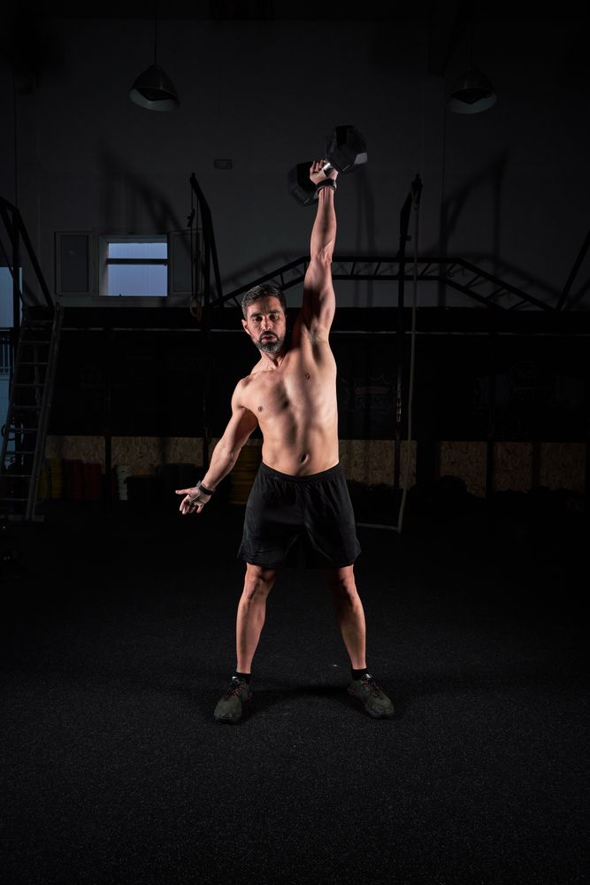 Sporty guy lifting dumbbell in dark fitness center
