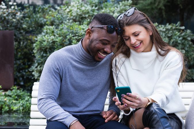 Joyful multiethnic couple listening music on smartphone in park