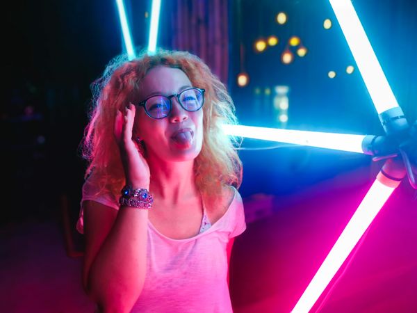 Portrait of woman poking her tongue and standing by neon light