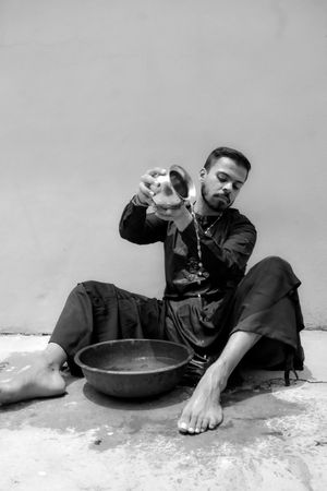 Grayscale photo of man wearing kurta pouring water on floor while sitting