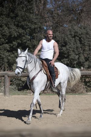 Man in sleeveless shirt riding horse on sandy ground