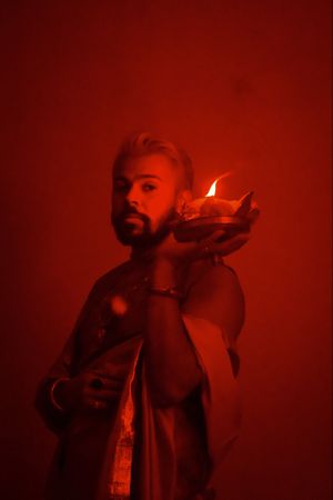 Portrait of Indian man in sari holding a diya in red lit studio