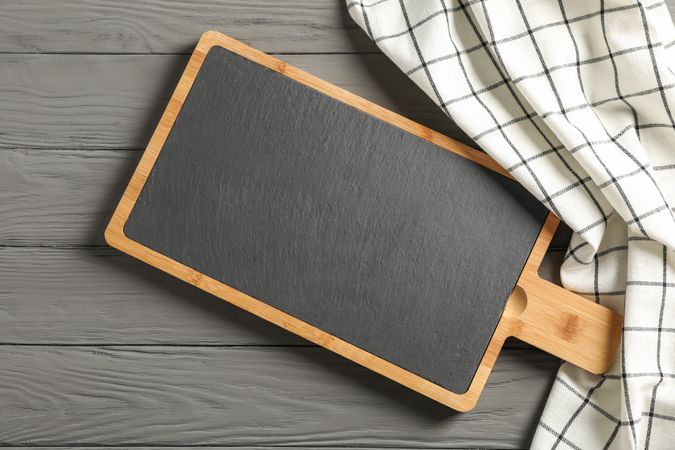 Kitchen towel with cutting board on wooden background, top view