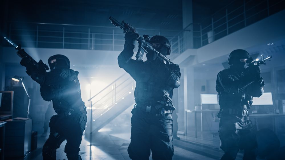 Masked Squad of Armed SWAT Police Officers Stand in Dark Seized Office Building with Desks and Computers.