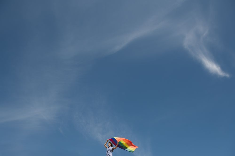 Young woman with rainbow banner against sky