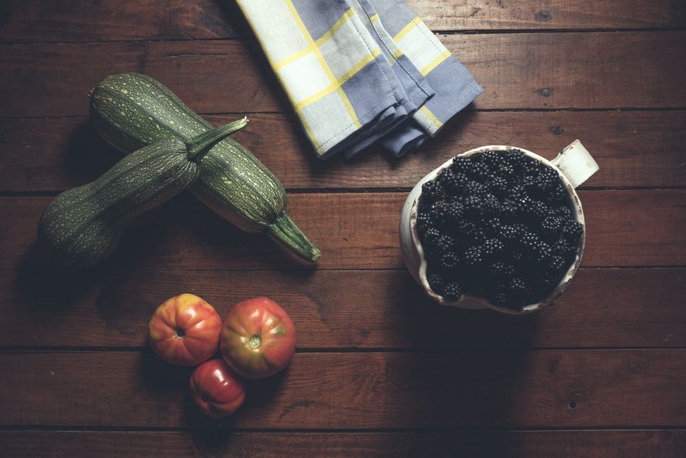 Ripe blackberries garnished by vegetables in bowl on wooden background