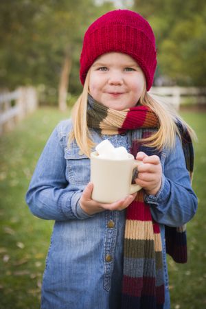 Cute Young Girl Holding Cocoa Mug with Marsh Mallows Outside