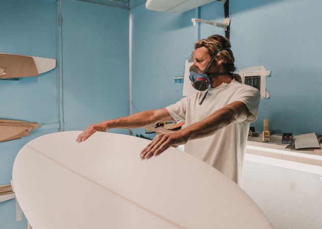 Man holding surf board on stand in workshop