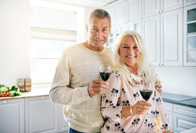 Portrait of mature couple smiling in bright kitchen with red wine