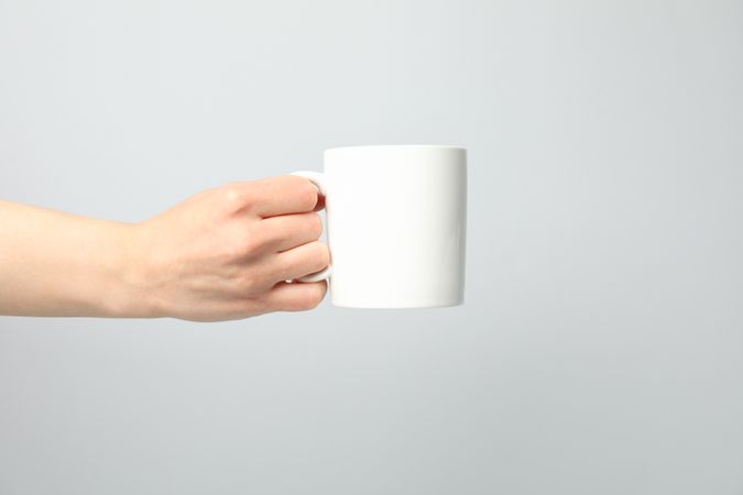 Female hand holding cup on light gray background, space for text