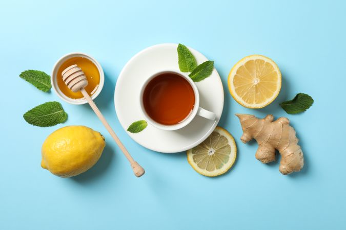 Flat lay. Cup of tea, lemon, ginger, mint, honey and dipper on blue background, copy space